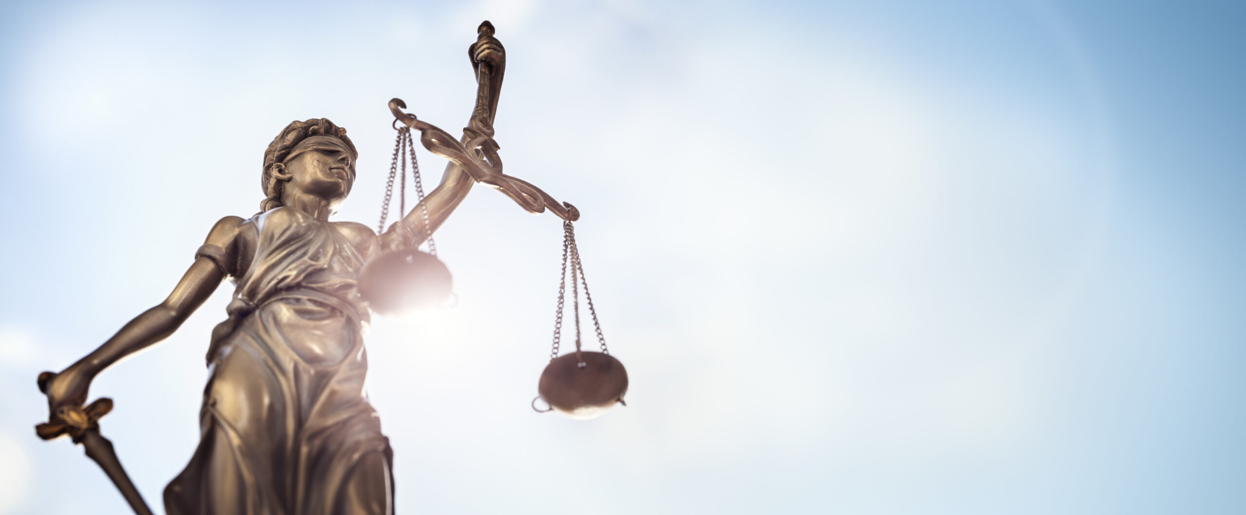 Statue of Lady Justice with scales of justice and sky in the background