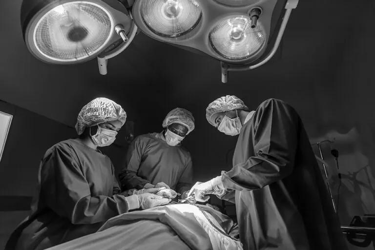 black and white image of surgeons in scrubs operating on a patient