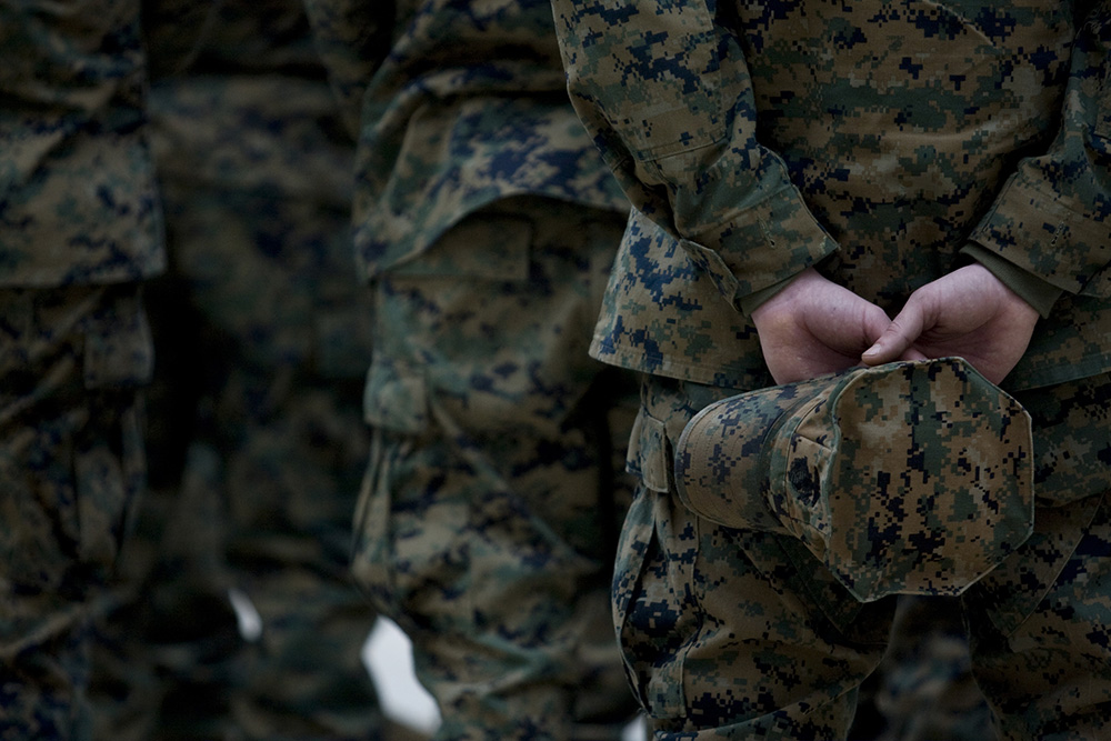 Line of Marines in camouflage with the last holding his cap in his hands behind his back