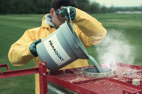 Farm worker dispenses paraquat into a piece of machinery