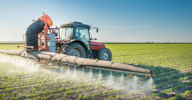 Heavy machinery crawls rows of crops spraying herbicide on them