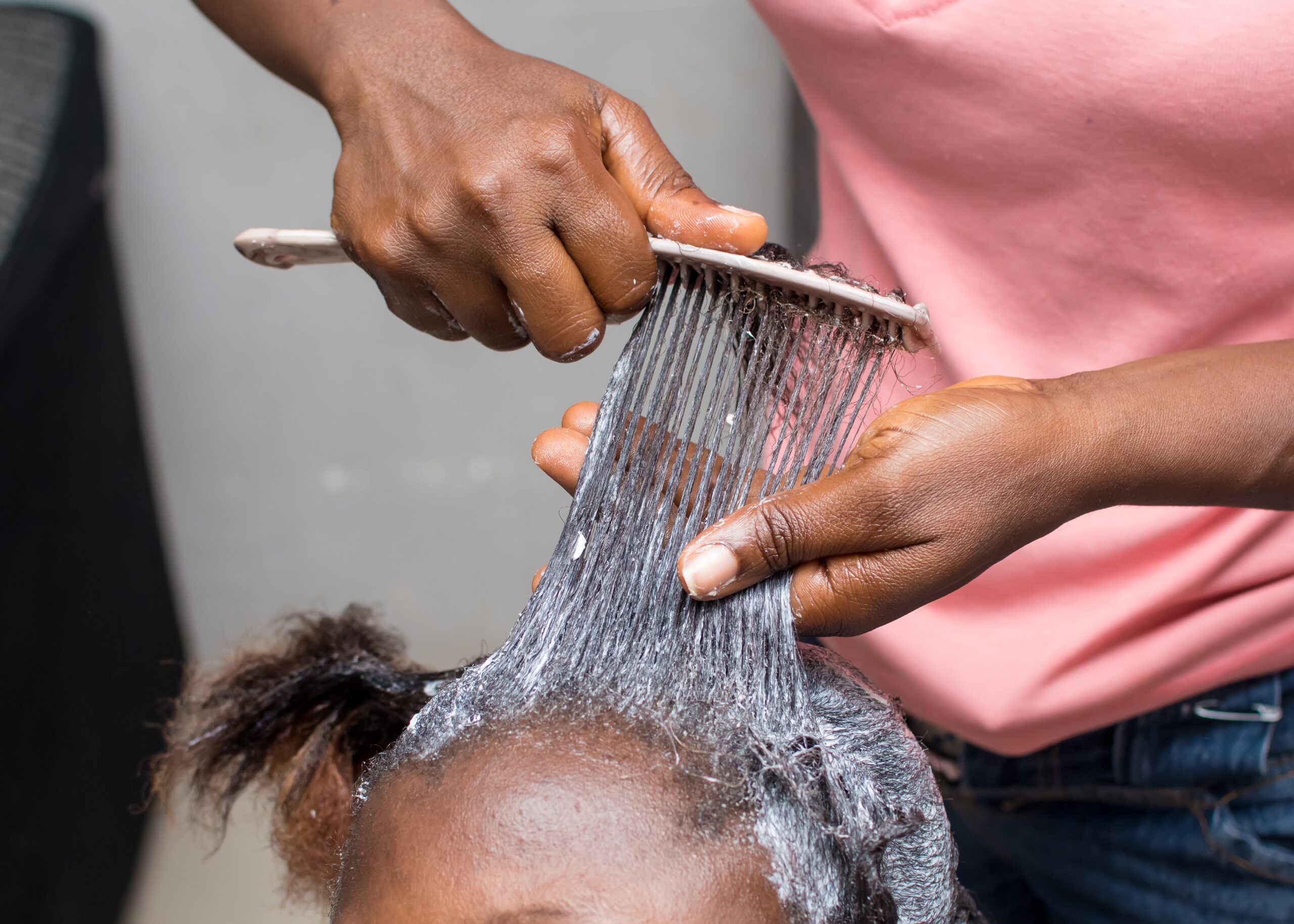 A woman seated while having hair relaxer applied by a salon professional