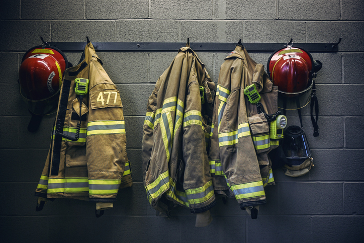 Fire turnout coats and helmets hang in a row on hooks